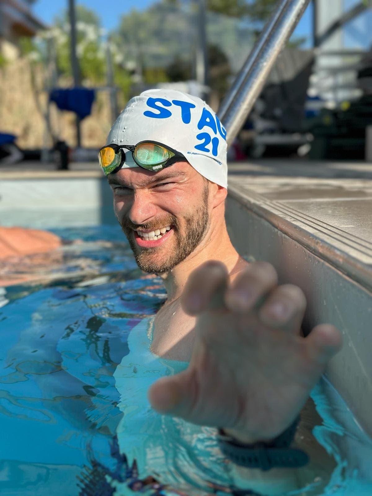Close-up of a swimmer in the sun, Stage 21 cap and goggles, blue pool water
